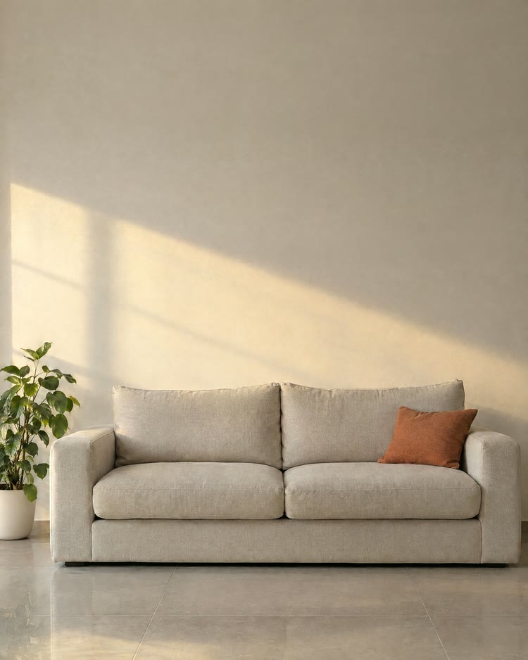 Una pared lisa color crema detrás de un sofá de lino, con luz de la tarde